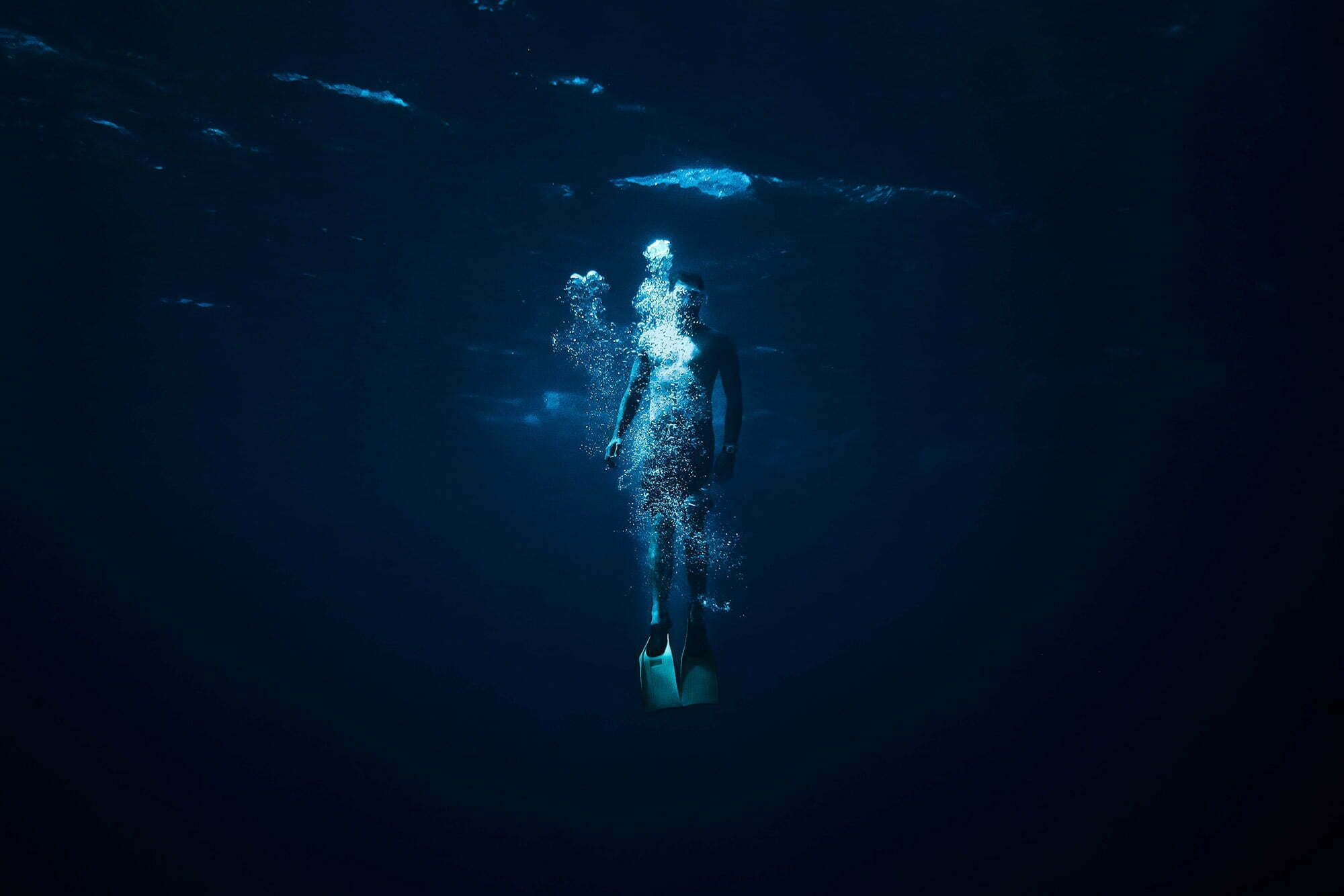 Person resurfacing from a dive in dark blue ocean water to take a breath